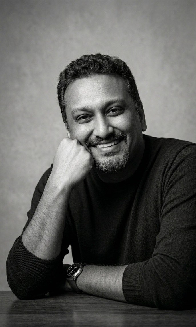 Black and white portrait of Anzar Khaliq, smiling, chin resting on his hand