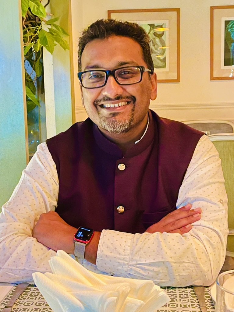 Anzar Khaliq at a dinner table, smiling, arms crossed